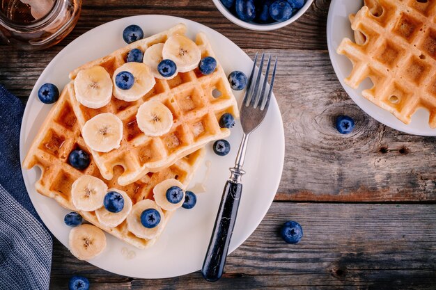 Verse zelfgemaakte Belgische wafels met bosbessen en banaan voor het ontbijt op houten achtergrond