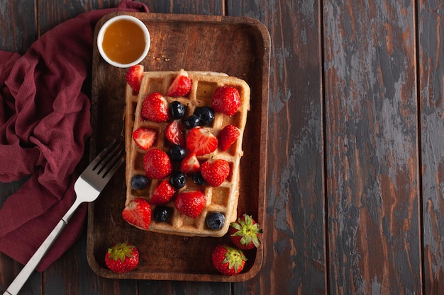 Foto verse zelfgemaakte belgische wafels op een oude houten tafel met frambozen bosbessen en honing