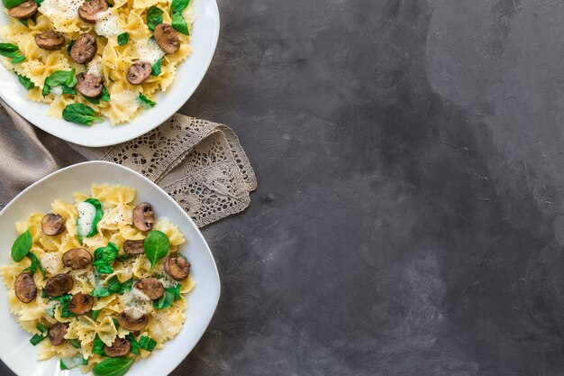 Verse zelfgemaakte farfalledeegwaren met champignons en spinazie op concrete achtergrond. Bovenaanzicht met ruimte voor tekst.