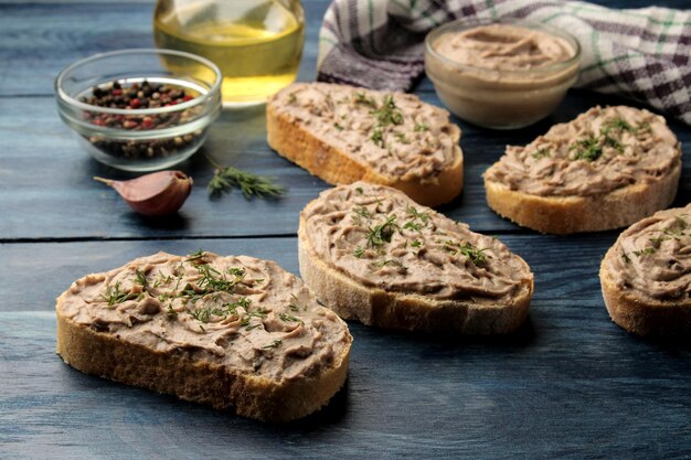 Verse zelfgemaakte kippenleverpastei met kruiden op brood op een blauwe houten tafel. Een sandwich.