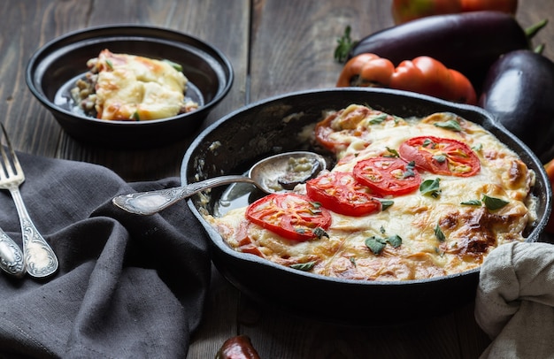 Verse zelfgemaakte moussaka in ijzeren koekenpan op rustieke houten achtergrond met ingrediënten. Griekse keuken.