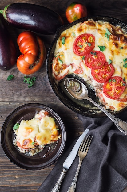 Foto verse zelfgemaakte moussaka in ijzeren koekenpan op rustieke houten achtergrond met ingrediënten