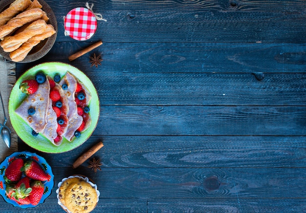 Verse zelfgemaakte pannenkoeken geserveerd op een bord met aardbeien en bosbessen, op een donkere houten achtergrond,