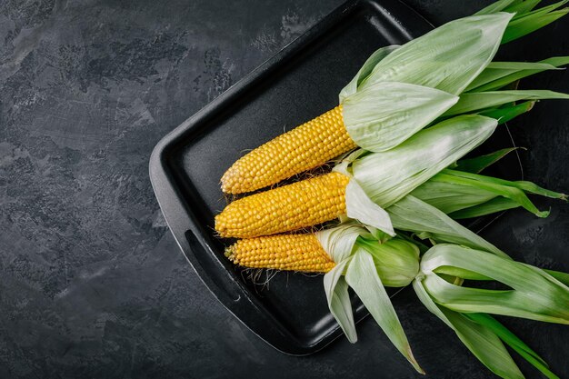 Verse zoete gouden maïskolven op donkergrijze stenen achtergrond bovenaanzicht