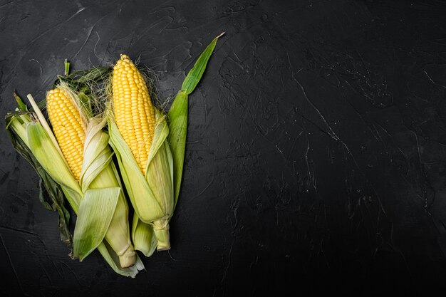 Verse zoete maïskolven set, op zwarte achtergrond, bovenaanzicht plat lag, met kopieerruimte voor tekst