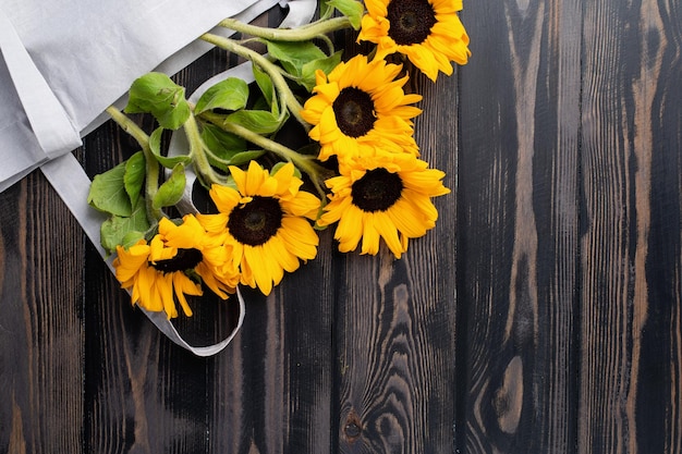 Verse zonnebloemen met bladeren op stengel in boodschappentas op houten achtergrond plat leggen bovenaanzicht kopie sp