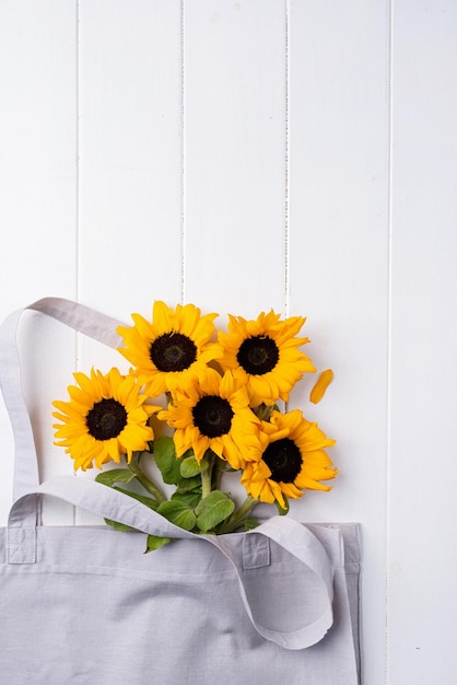 Verse zonnebloemen met bladeren op stengel in boodschappentas op houten achtergrond plat leggen bovenaanzicht kopie sp