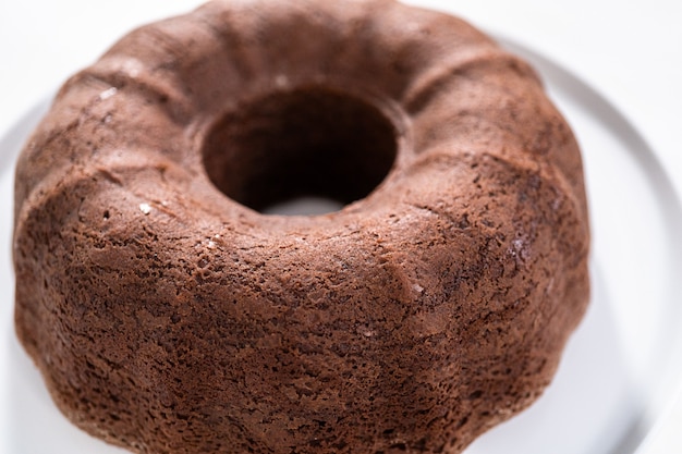 Versgebakken chocolade bundt cake op een witte taart staan.