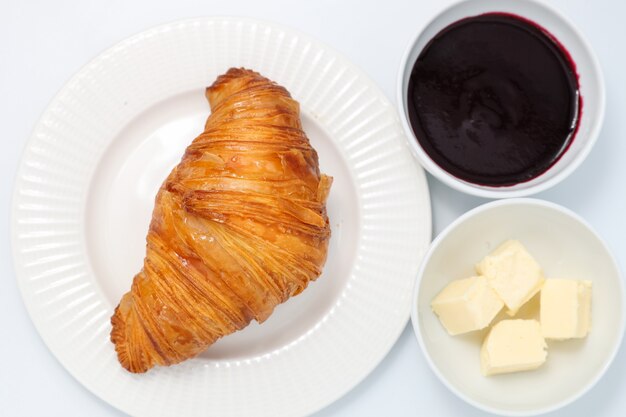 Versgebakken croissant, jam en boter plakjes op een lichte achtergrond