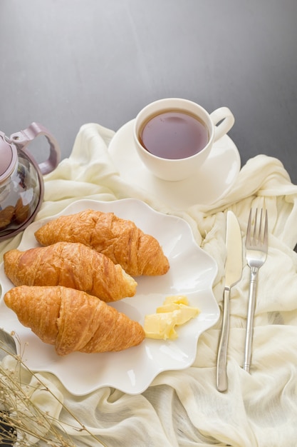 Versgebakken croissants en kopje thee op een witte plaat op een donkere tafel achtergrond