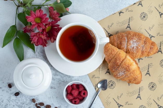 Versgebakken croissants met een kopje thee en zoet fruit.