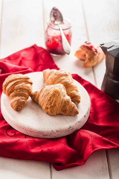 Versgebakken Franse croissants met een potje jam op een lichte houten ondergrond met een rood servet.