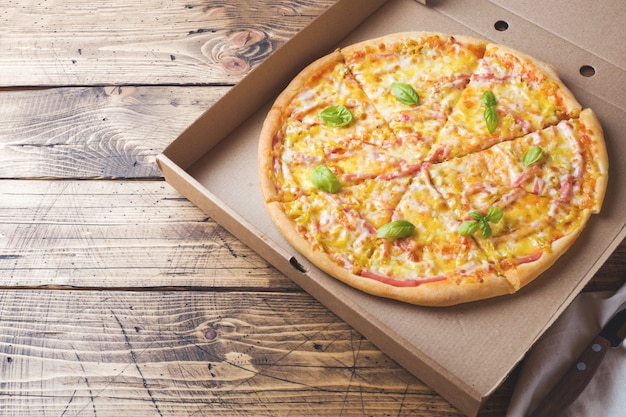 Versgebakken pizza in een kartonnen doos op een houten tafel.