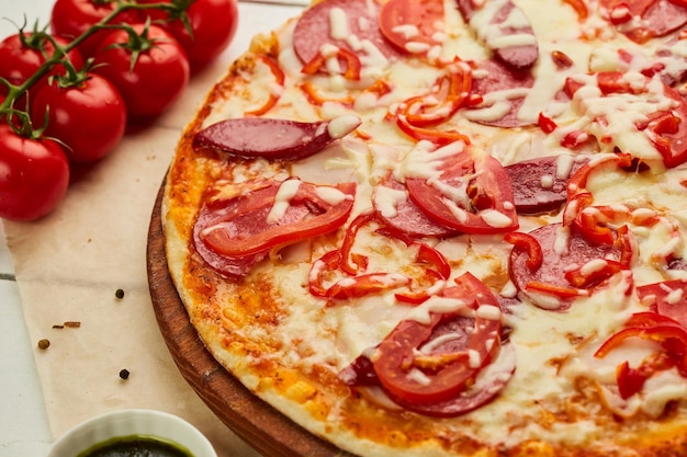 Versgebakken pizza met gerookte worst, rode peper en tomaten geserveerd op houten ondergrond met saus en kruiden Voedselleveringsconcept Restaurantmenu