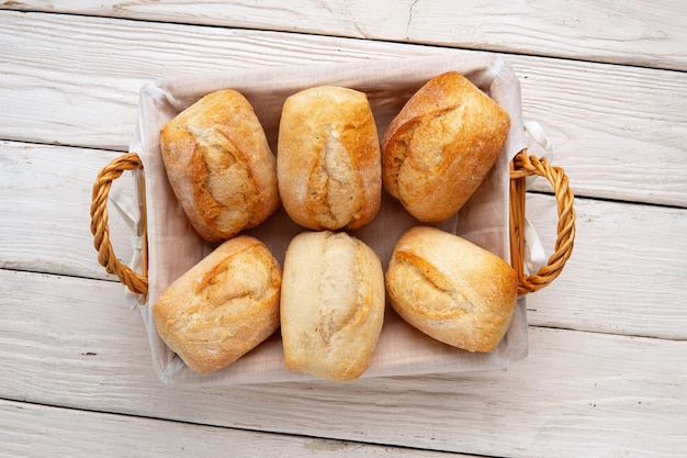 Versgebakken tarwebroodjes in een rieten mand op witte houten tafel