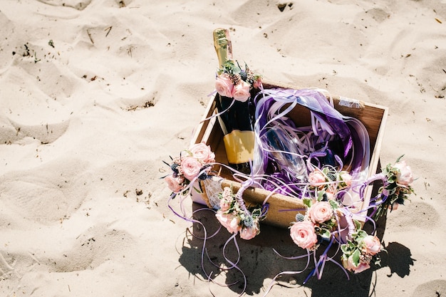 Versierde doos met champagnewijn en glas Decor van bloemen op het zand op het strand Plaats voor tekst Close-up natuur Stijl boho Feest Maiden avond Vrijgezellenfeesten Vrijgezellenfeest