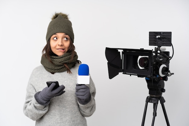 Verslaggever vrouw die een microfoon vasthoudt en nieuws rapporteert over geïsoleerd wit met koffie om mee te nemen en een mobiel terwijl ze iets denkt