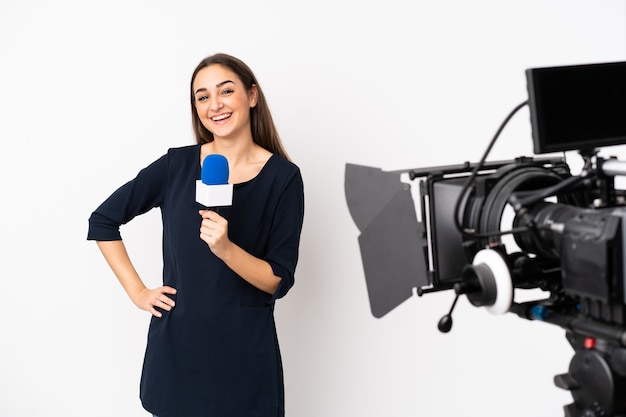 Verslaggever vrouw met een microfoon en rapportage nieuws geïsoleerd op een witte achtergrond poseren met armen op heup en glimlachen