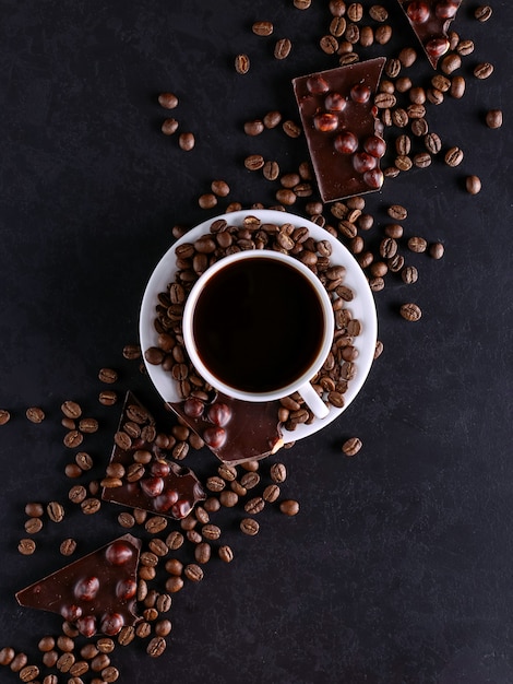 Verspreide koffiebonen, een kop en zwarte chocolade op een zwarte stenen tafel. Ruimte kopiëren.