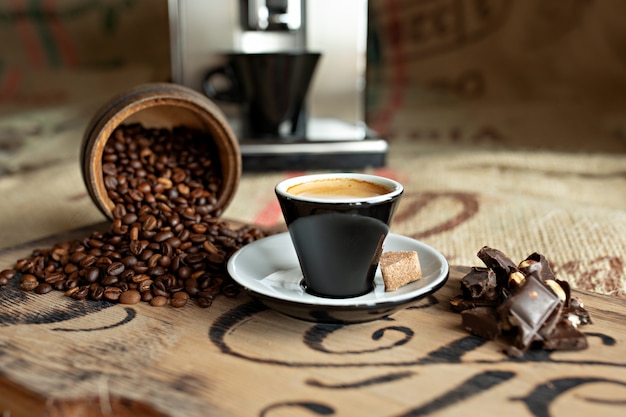 Verspreide koffiebonen, een kopje espresso, stukjes chocolade met noten op een houten bord.