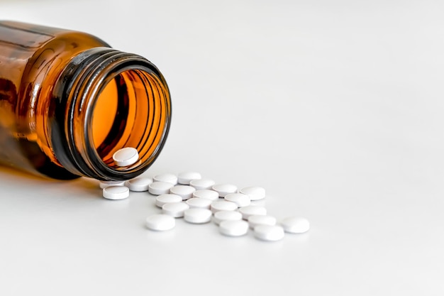 Verspreide witte ronde vitaminen en bruine glazen fles op witte achtergrond kopieer ruimte close-up