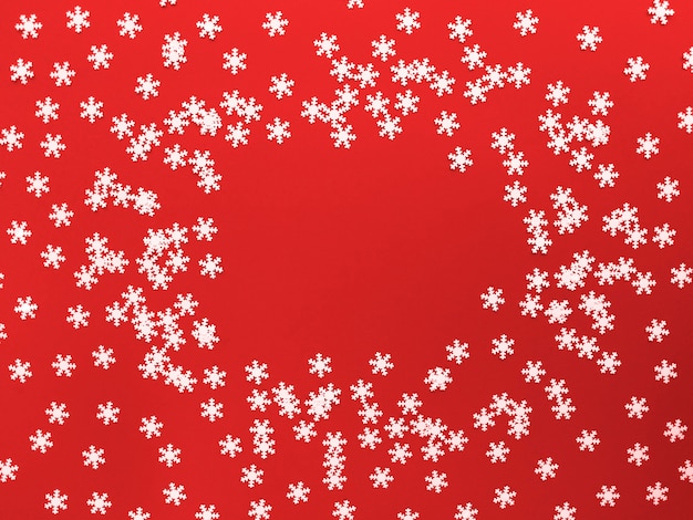 Verspreide witte sneeuwvlokken op rode achtergrond. Eenvoudig plat leggen met kopie ruimte.