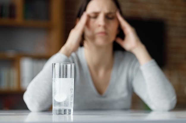 Verstoorde jonge vrouw die lijdt aan hoofdpijn die oplosbaar medicijn gebruikt voor pijnverlichting Uitgeputte vrouw met pijnlijke gevoelens Migraine hoge bloeddruk chronische vermoeidheid en vermoeide ogen