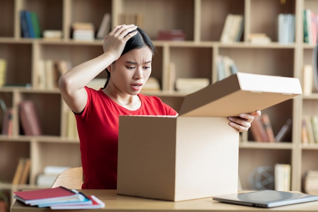 Verstoorde ongelukkige tiener Aziatische vrouw kijkt naar kartonnen doos in het interieur van de woonkamer