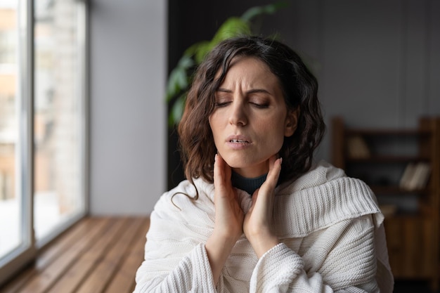 Verstoorde zieke vrouw die thuis staat en gezwollen klieren aanraakt die lijden aan angina of tonsillitis