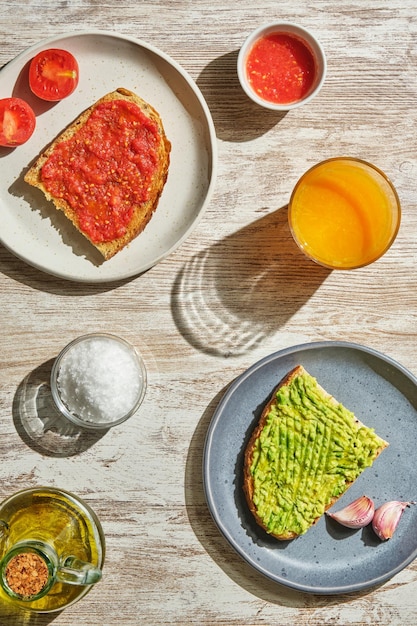 Verticaal beeld van bovenaf van toast met tomaat, avocado, toast, zout, olijfolie en jus d'orange
