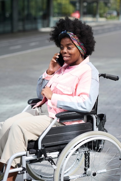 Verticaal beeld van een Afro-Amerikaanse vrouw met een handicap die buiten aan de telefoon praat