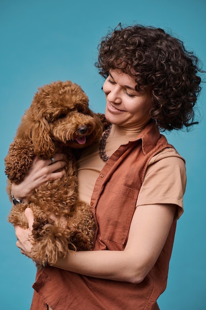 Verticaal beeld van een gelukkige jonge eigenaar die haar hond in haar armen houdt en tegen een blauwe achtergrond staat