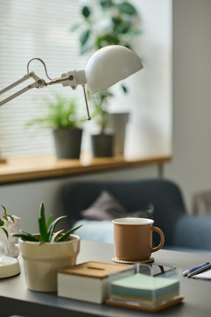 Verticaal beeld van werkplek met warme drank op tafel tijdens koffiepauze thuis