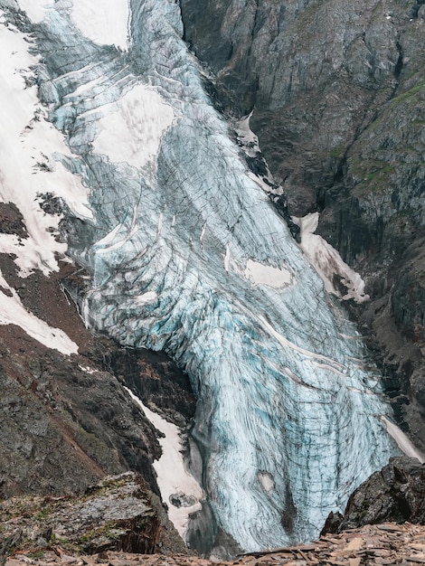 Verticaal berglandschap met blauwe lange verticale gletsjertong met scheuren tussen rotsen Luchtfoto naar grote gletsjer met ijsval Aardtextuur van berggletsjer met scheuren close-up