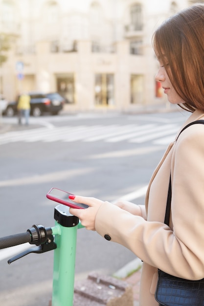 Verticaal bijgesneden shot van een vrouw die de qr-code van een elektrische scooter scant, om het voertuig te huren voor een ritje