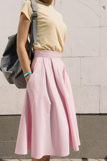 Verticaal bijsnijden van het meisje in het gele shirt, roze rok en rugzak tegen de muur