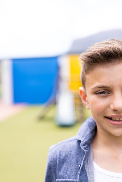 Verticaal half gezicht portret van glimlachende blanke schooljongen in schoolplein met kopieerruimte