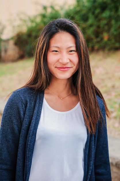 Foto verticaal individueel portret van een jonge chinese vrouw die glimlacht en naar de camera kijkt.