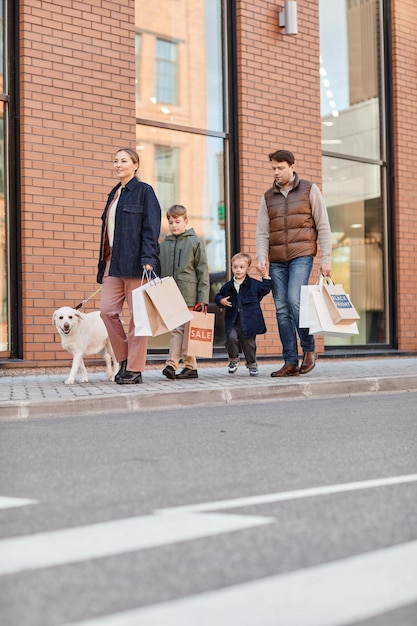 Verticaal portret over de volledige lengte van een moderne grote familie die een winkelcentrum verlaat met papieren zakken