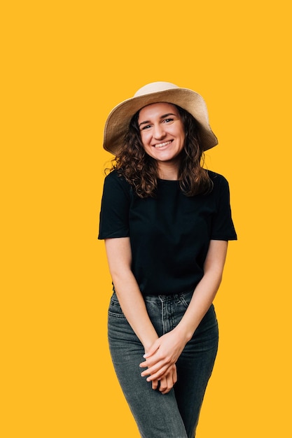 Foto verticaal portret over gele achtergrond van lachende verlegen vrouw met zomerhoed