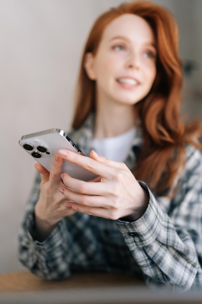 Verticaal portret van aantrekkelijke roodharige vrouw in casual kleding met behulp van smartphone chatten met