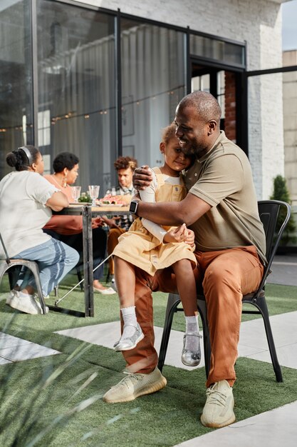 Verticaal portret van de volledige lengte van een gelukkige Afro-Amerikaanse man die een klein meisje omhelst tijdens de familiebijeenkomst...