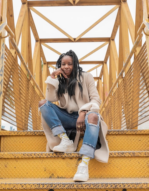 Verticaal portret van een Afro-Amerikaanse vrouw die op een trap van een gele brug zit met haar hand op haar gezicht