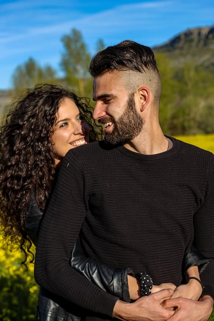 verticaal portret van een gelukkig paar dat in elkaars armen lacht en elkaar aankijkt in een veld met bloemen in de lente