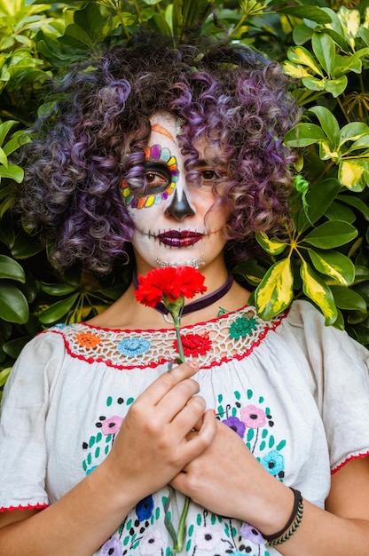 Verticaal portret van een jonge vrouw die een bloem vasthoudt met haar gezicht geschilderd als La Calavera Catrina