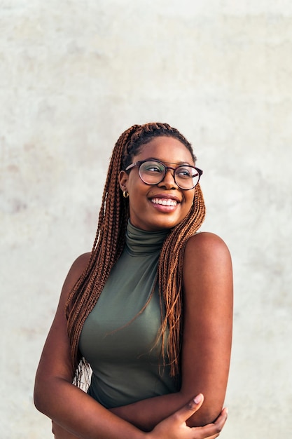 Verticaal portret van een jonge zwarte vrouw met een bril die lacht blij met een grijze betonnen muur op de achtergrond, concept van jeugd en raciale diversiteit, kopieer ruimte voor tekst