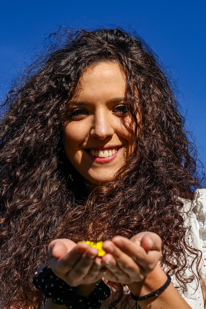 Verticaal portret van een mooie jonge vrouw die lacht en naar de camera kijkt met gele bloemblaadjes in haar hand