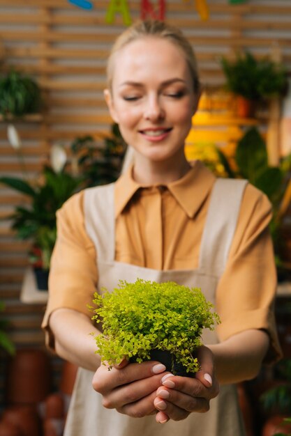 Verticaal portret van een mooie vrouwelijke bloemist in een schort die een pot in handen houdt met een Soleirolia-plant die in de bloemenwinkel staat en naar beneden kijkt