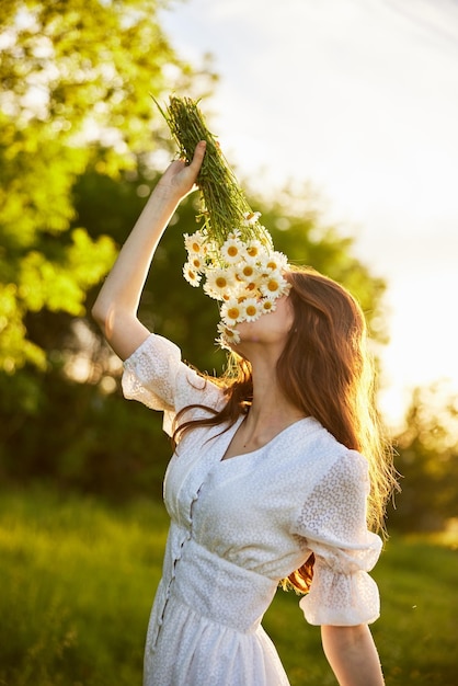 verticaal portret van een roodharige vrouw in de natuur tijdens zonsondergang die een boeket madeliefjes ruikt