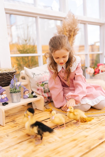 Foto verticaal portret van een schattig klein meisje in een jurk dat speelt met kleine gele eendjes die op de vloer zitten